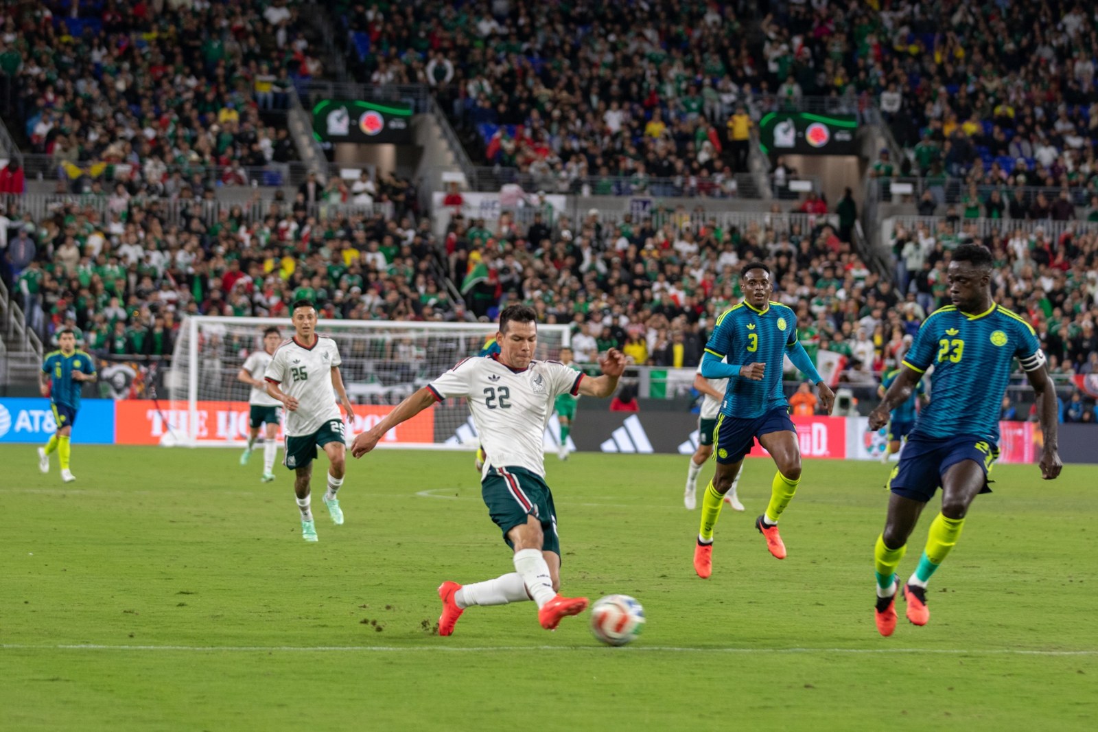 Mexico strikes the ball as Colombia closes in.