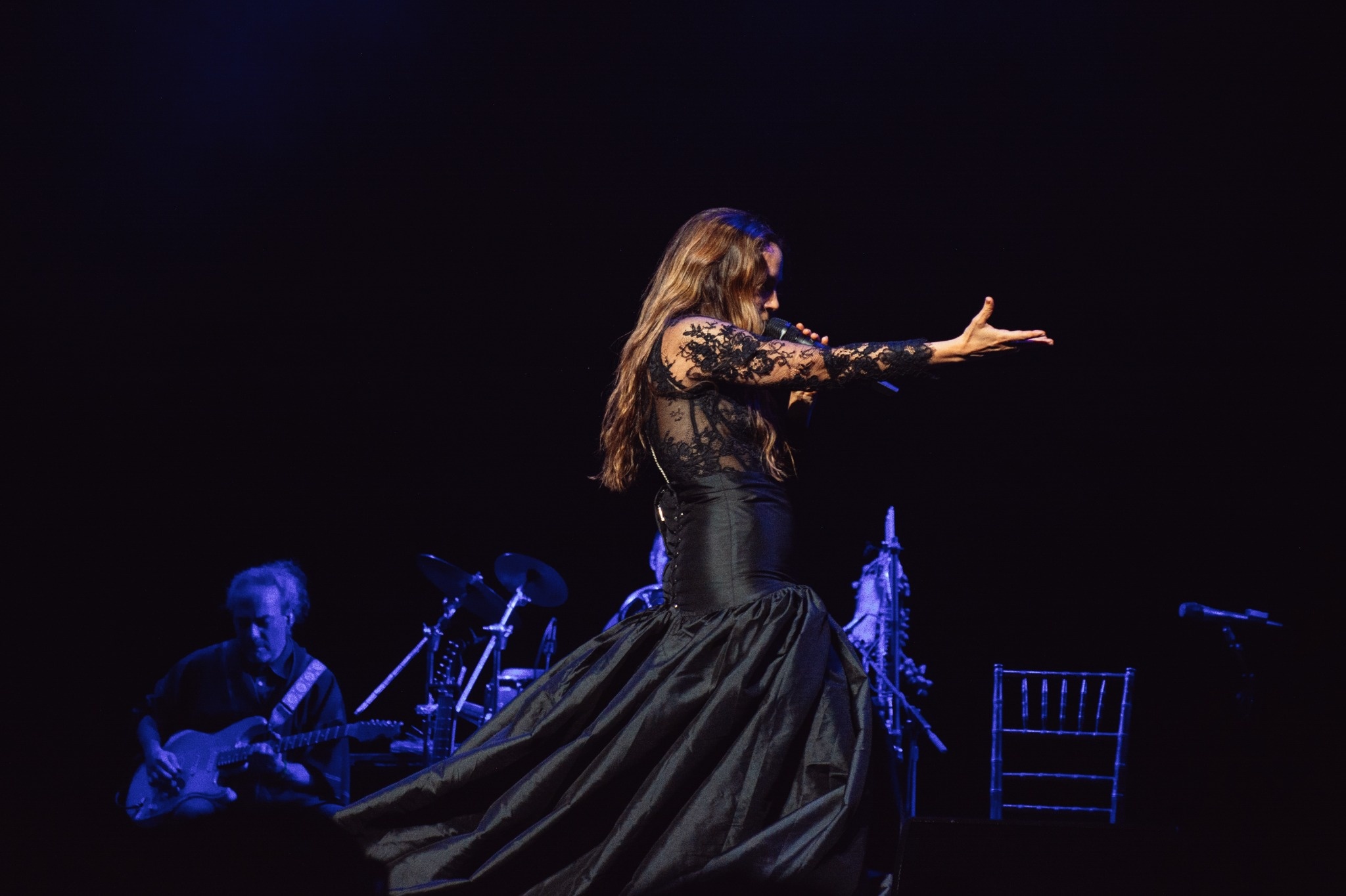 Natalia Lafourcade extending one arm as her black skirt moves onstage.