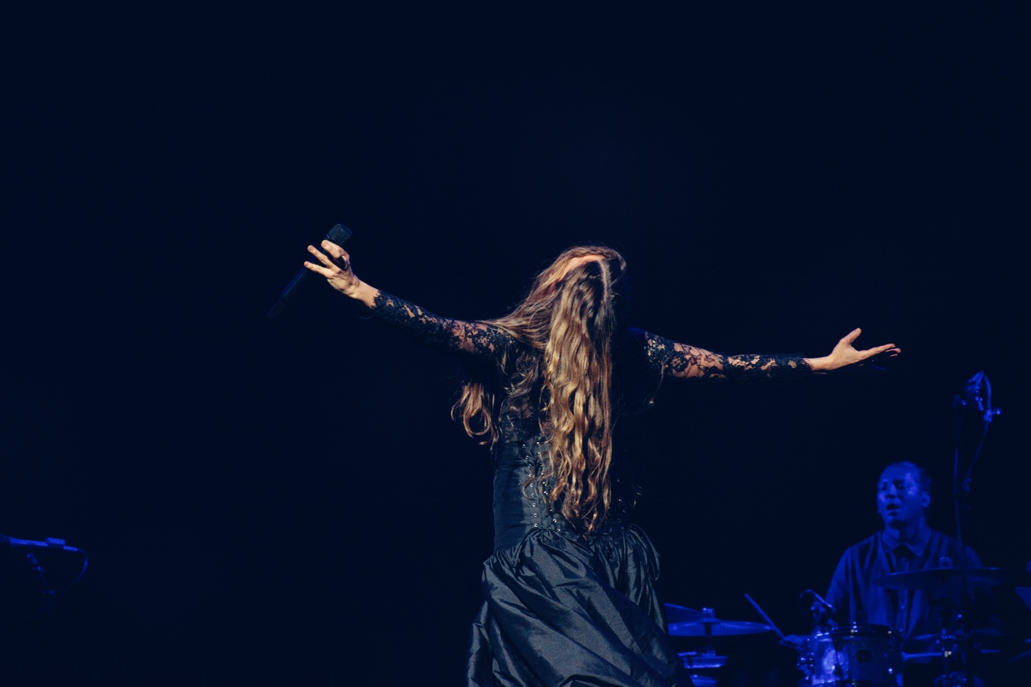 Natalia Lafourcade with her arms extended under blue stage lighting.