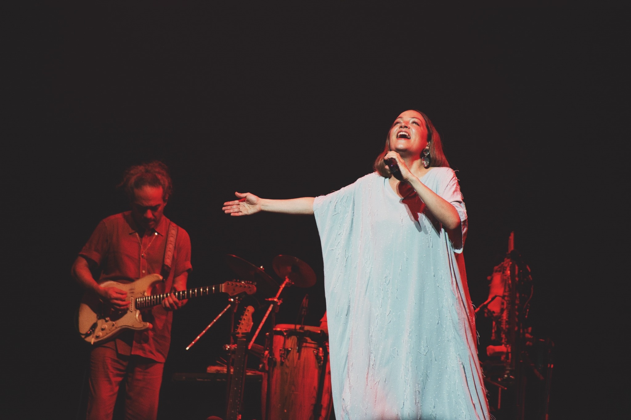 Natalia Lafourcade singing with one arm extended in a pale dress.