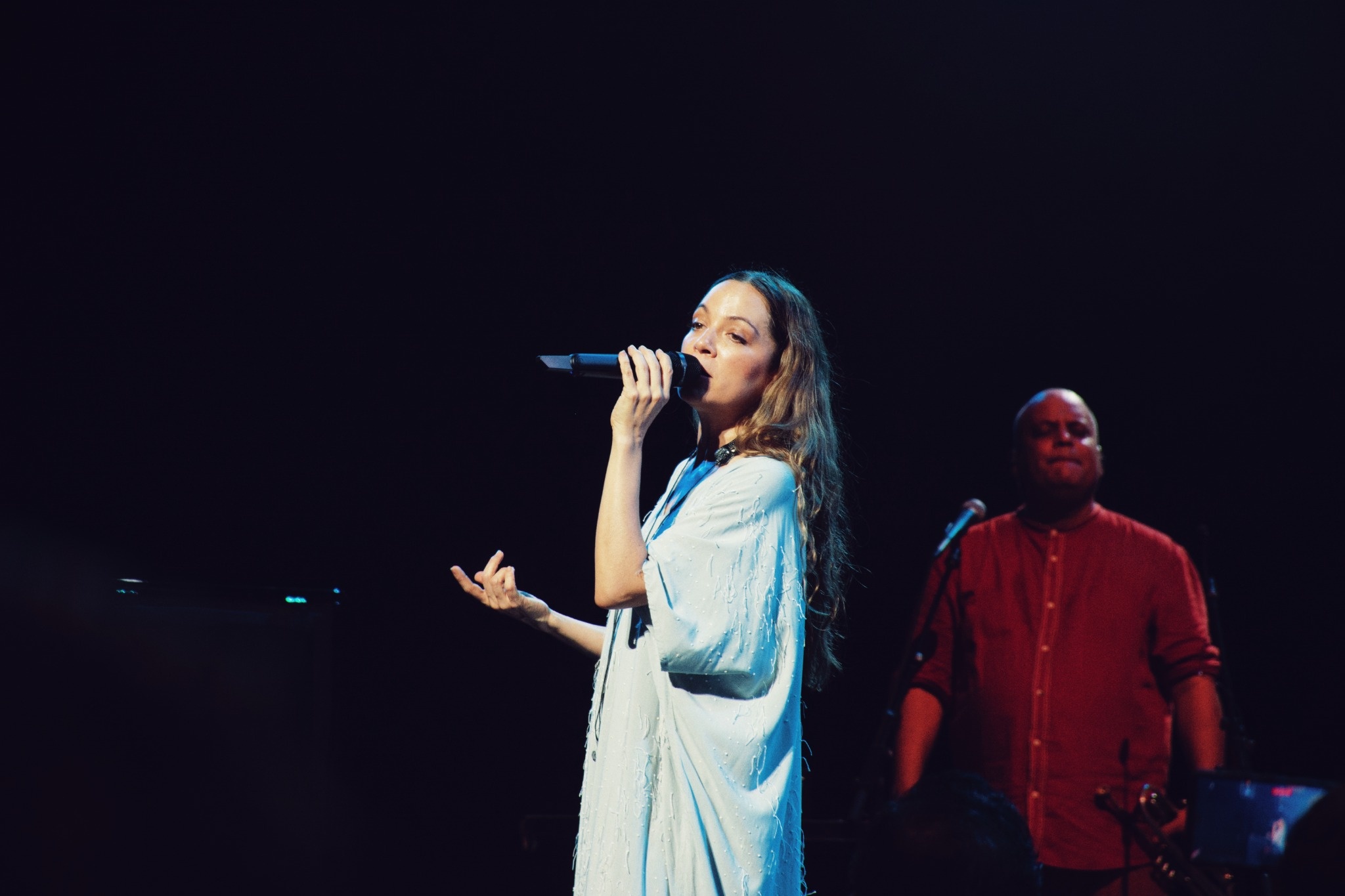 Natalia Lafourcade singing under blue light with a musician behind her.