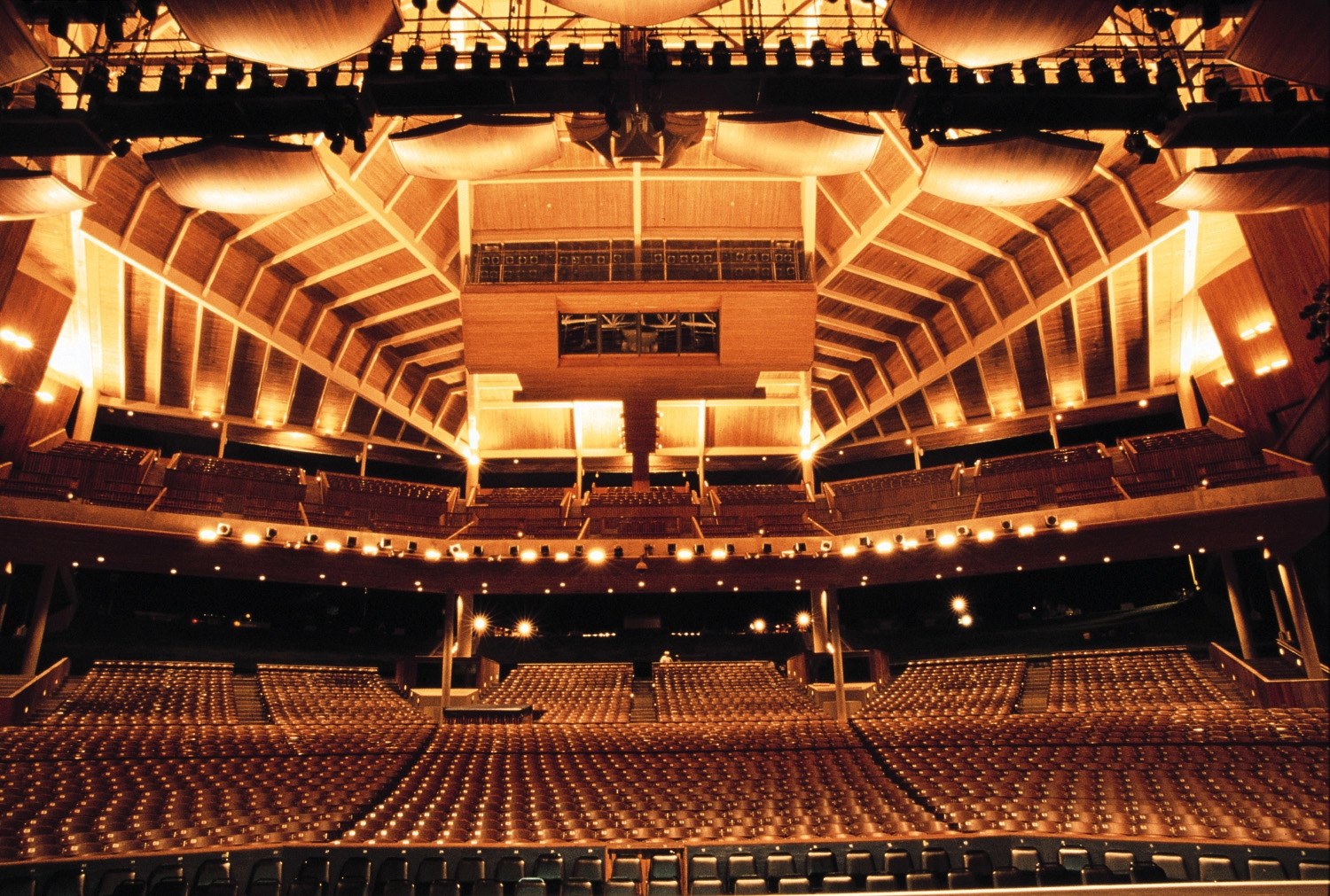 Warmly lit Filene Center interior with empty seats beneath wooden roof beams.